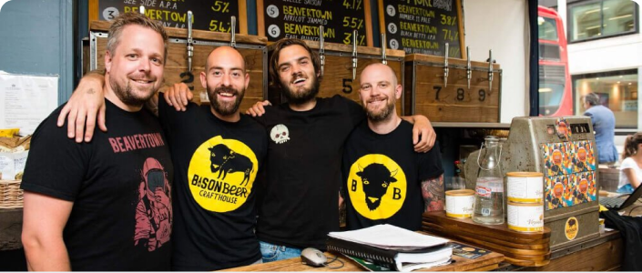 Staff of Bison Beer Crafthouse smiling and posing with their arms around each other behind the bar of their establishment.